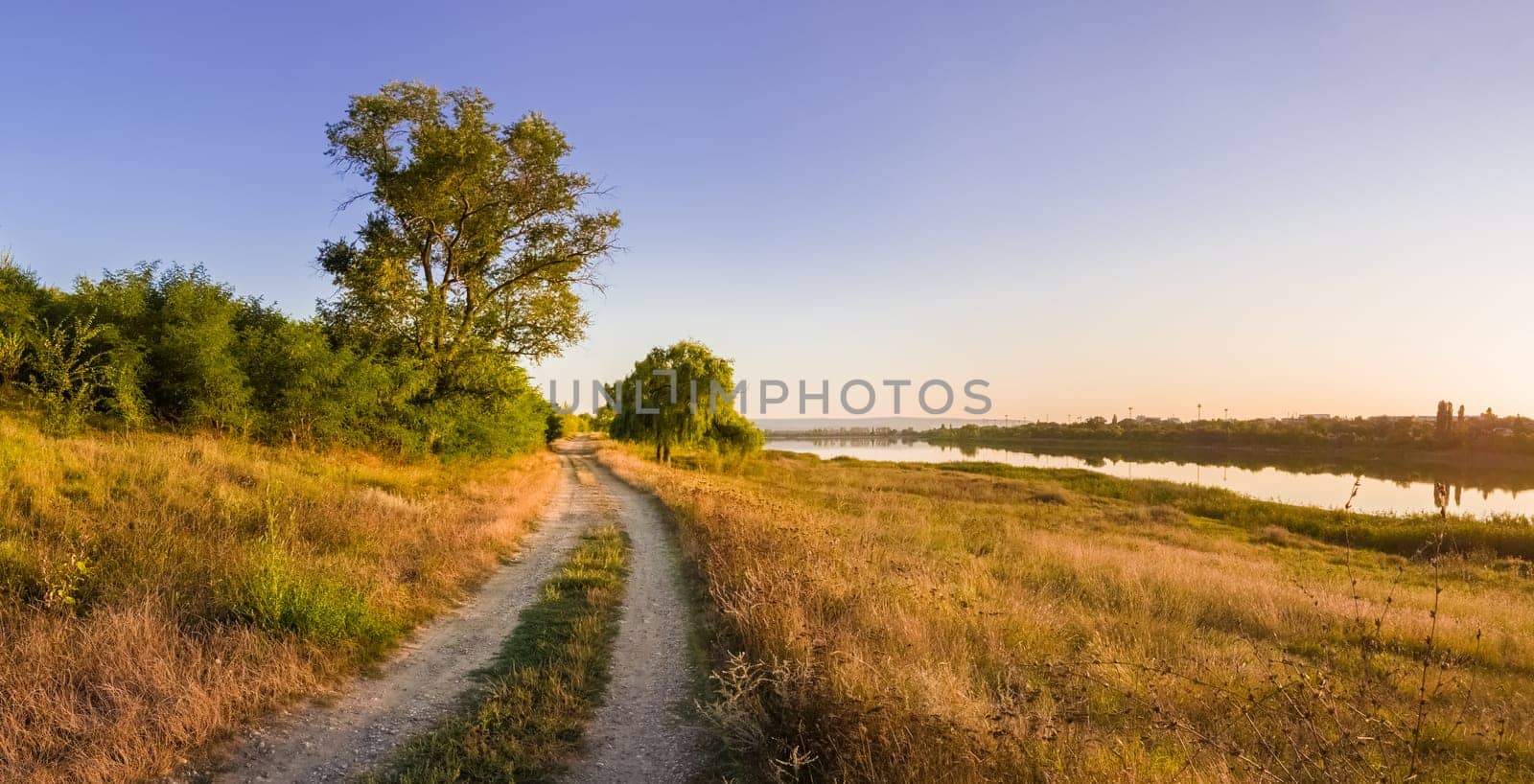 Scenic countryside landscape with rural dirt road across a meadow with dry grass and hay under a clear blue sky. Autumn panorama view near Delia lake, Ungheni, Moldova.