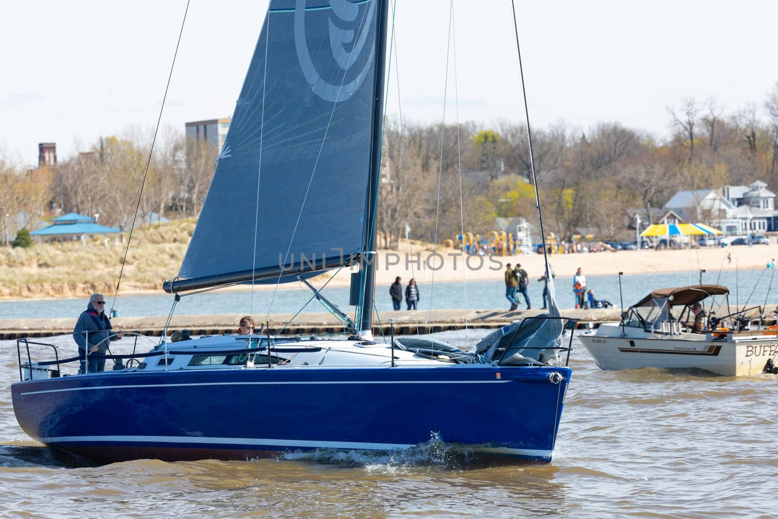 St. Joseph, Michigan, USA - May 4, 2019: Sail Boat leaving the harbor from St Joseph River and entering the Michigan Lake, passing by a fishing boat