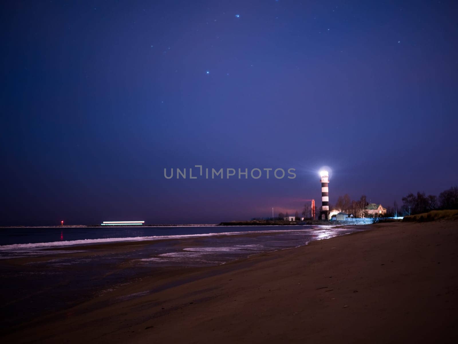 Black and white lighthouse at night in Baltic sea beach with stars