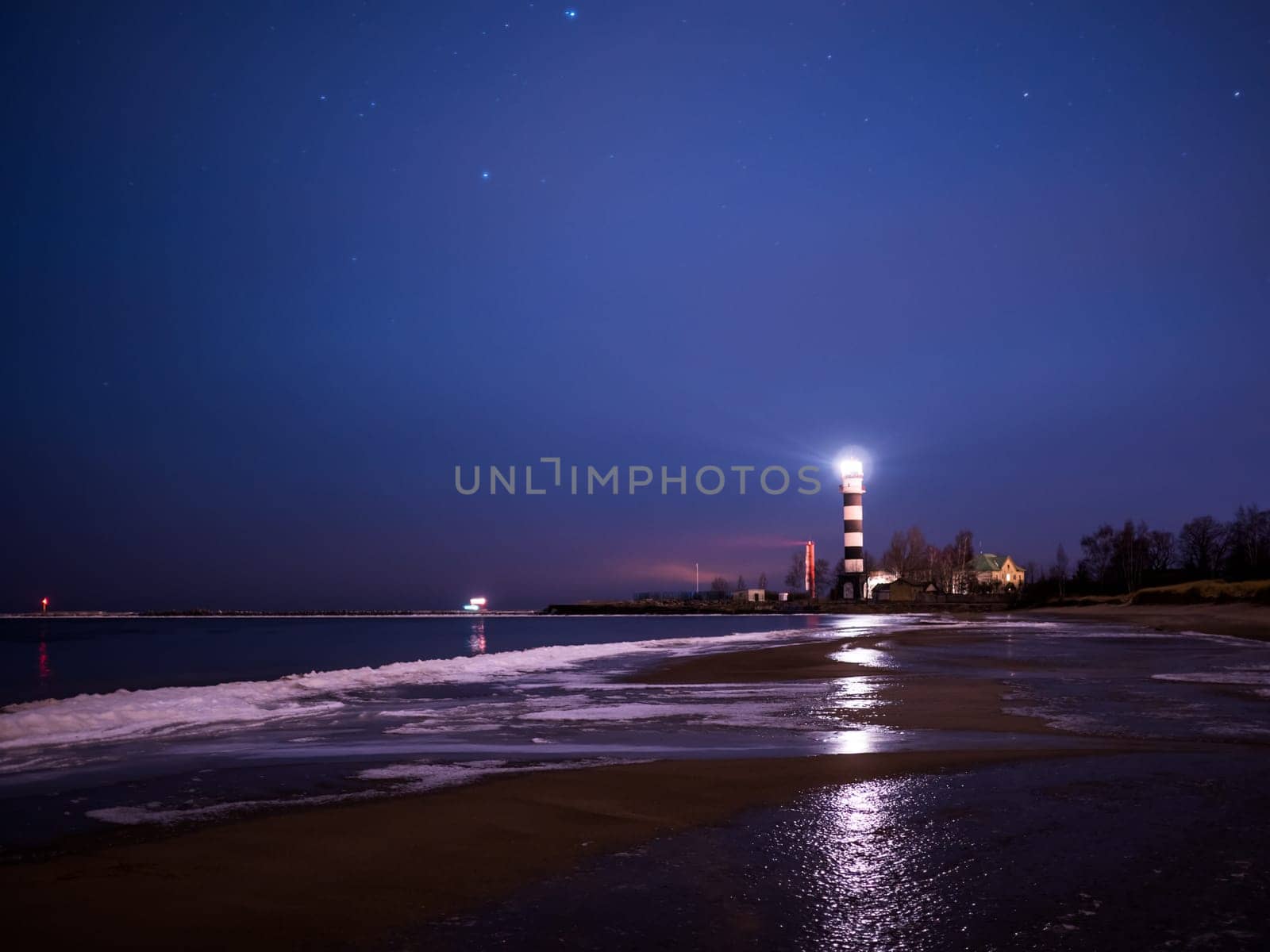 Black and white lighthouse at night in Baltic sea beach with stars