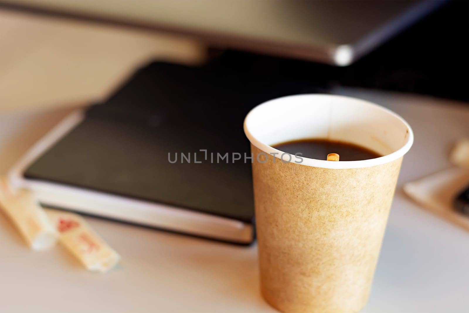 Hot coffee in a recycled paper container. Coffee break in the office. Closed book on the blurred background