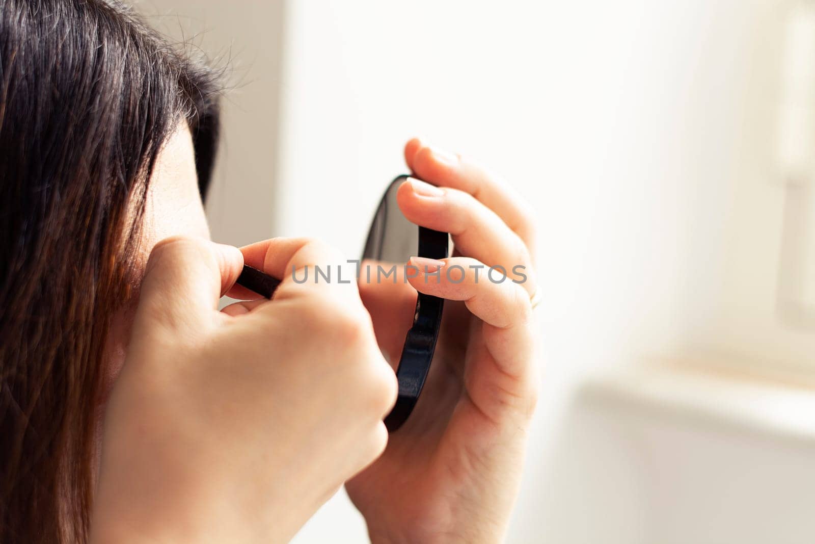 Female person using tweezers and a mirror with natural light. Personal care and beauty. Makeup accessories