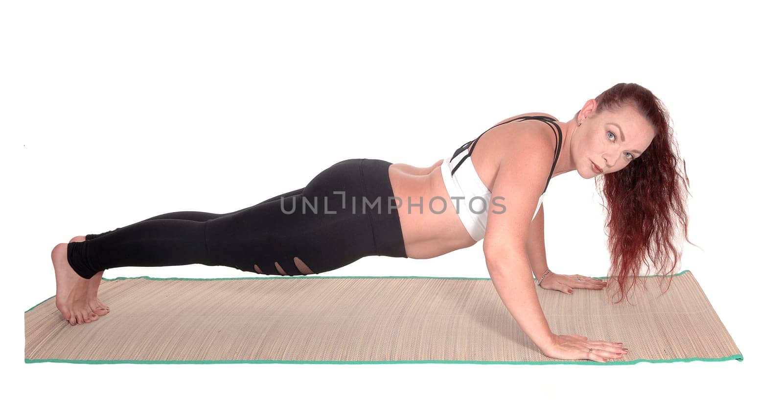 A middle age woman in sports outfit doing push ups on a mads.with her red hair and nice figure, isolated for white background.