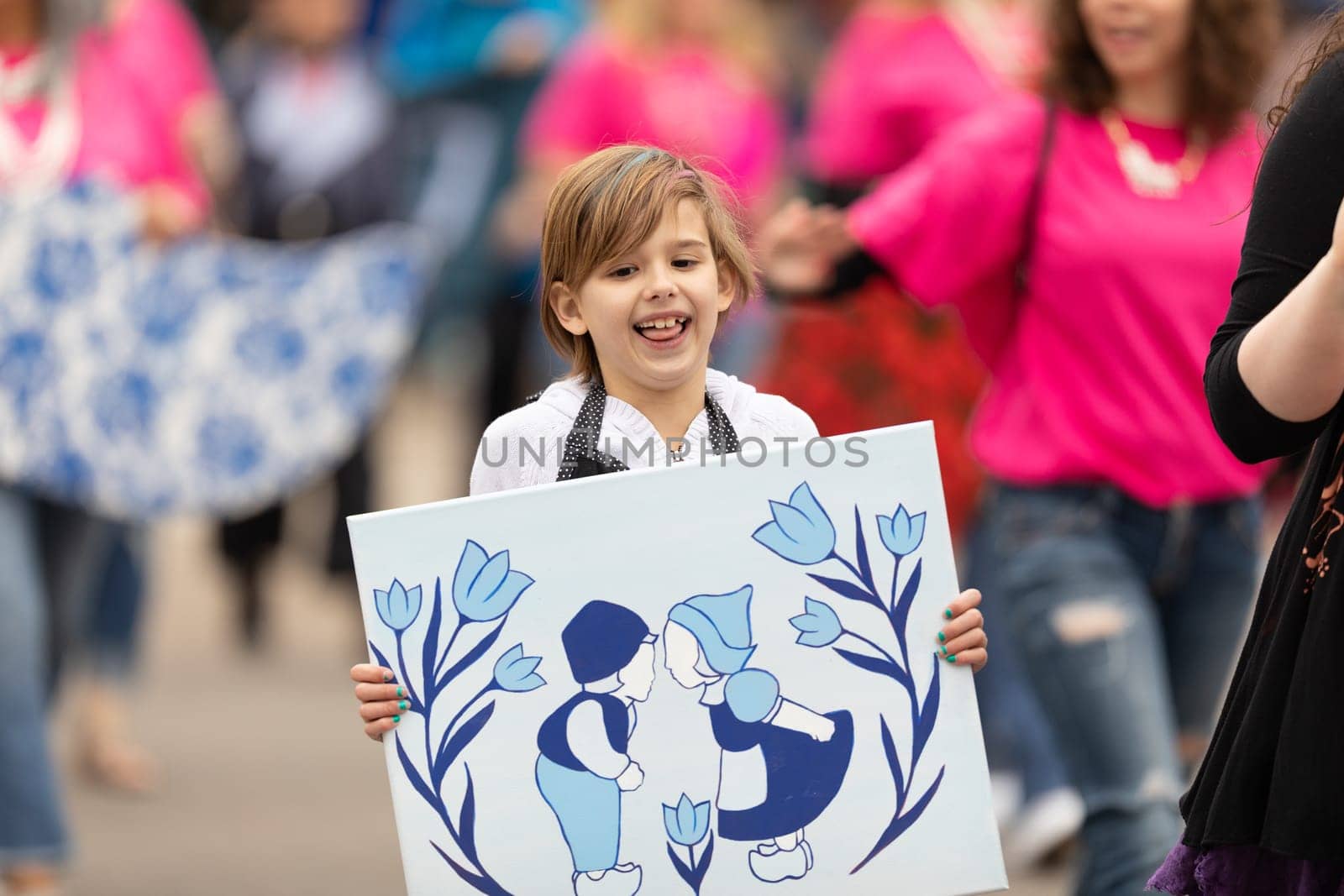 Holland, Michigan, USA - May 11, 2019: Tulip Time Parade, Woman accompanying children displaying their dutch related artworks during the parade