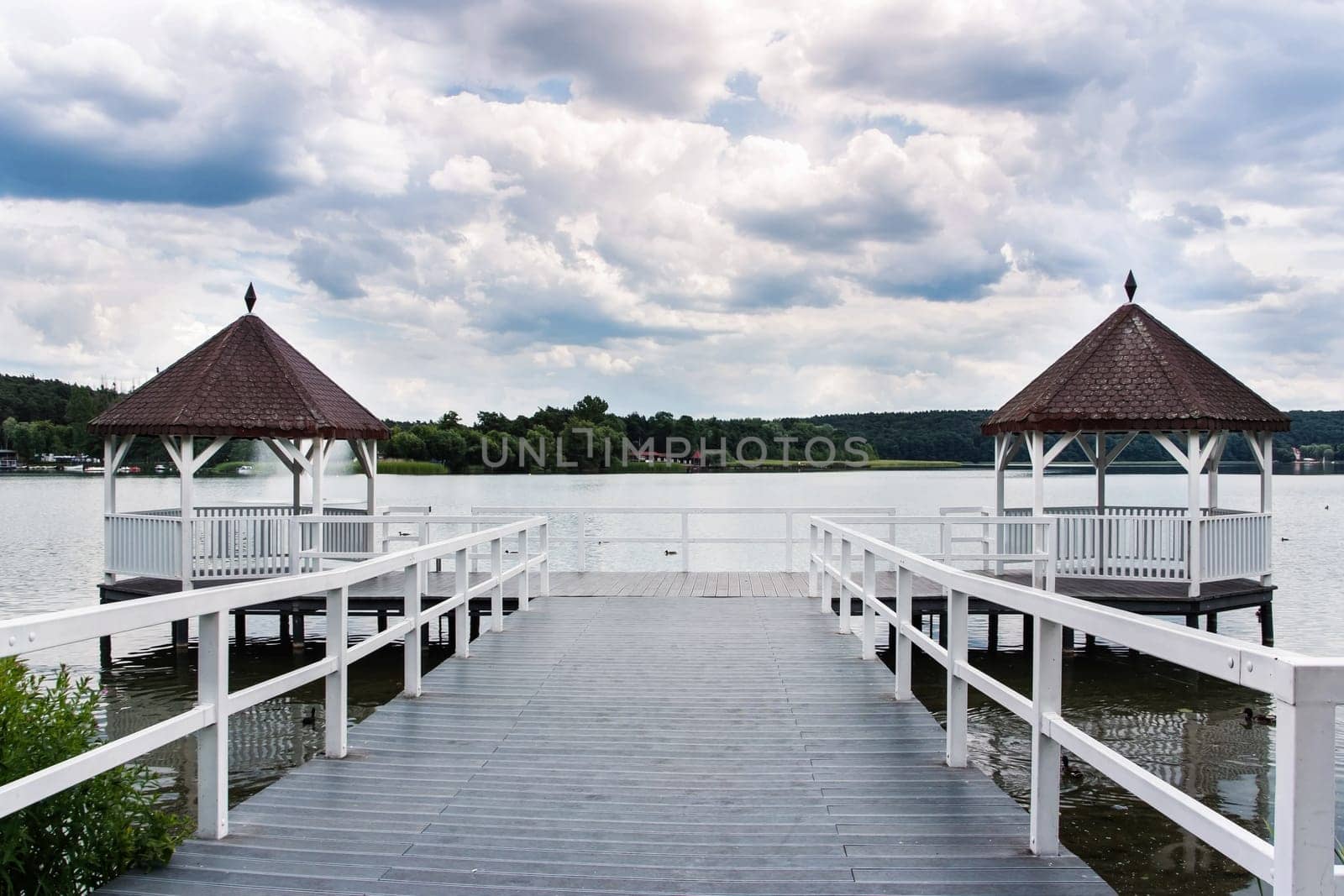 Beautiful white roofed pier with wooden huts on lake, green forest and puffy clouds in background, Barlinek, Poland