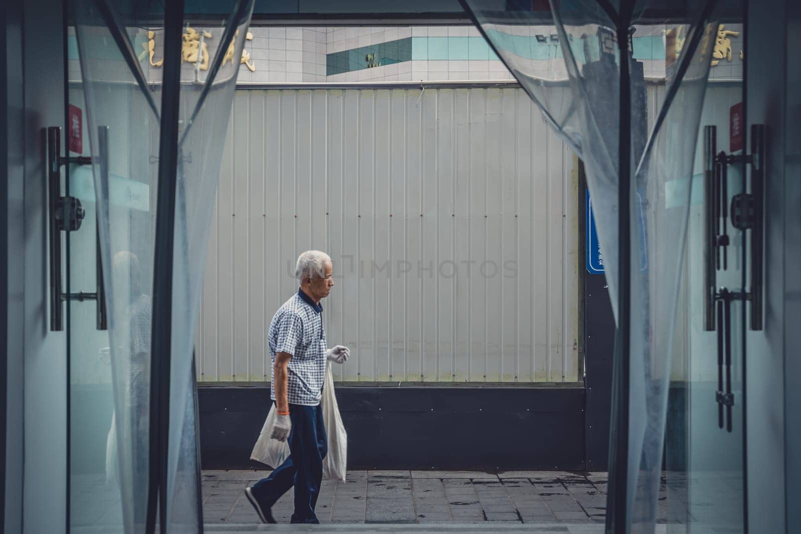 Xian, China -  July 2019 : Old chinese man walking on a street in Xian, photographed from the inside of a shop