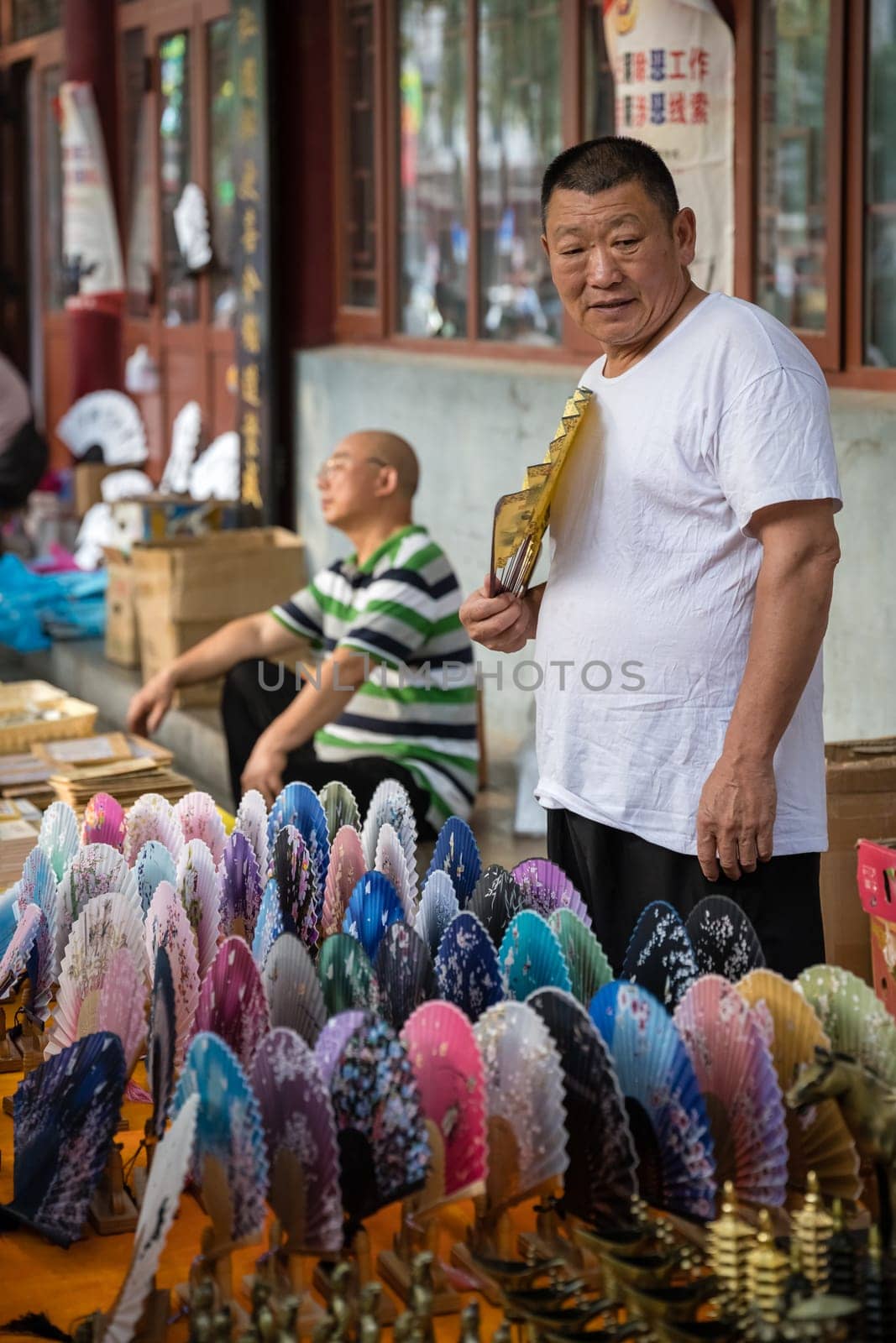 Xian, China -  July 2019 : Older man selling colorful paper fans on a hot day on the street in the Muslim Quarter