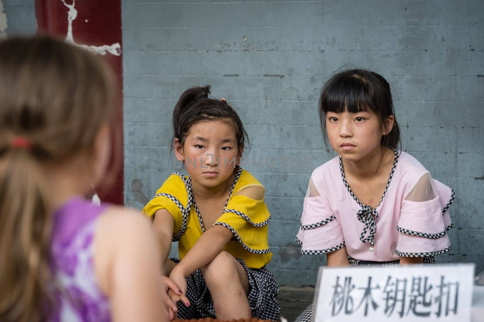 Xian, China -  July 2019 : Two little Chinese girls looking at a Caucasian girl standing in front of a souvenir stand on the street in the Muslim Quarter