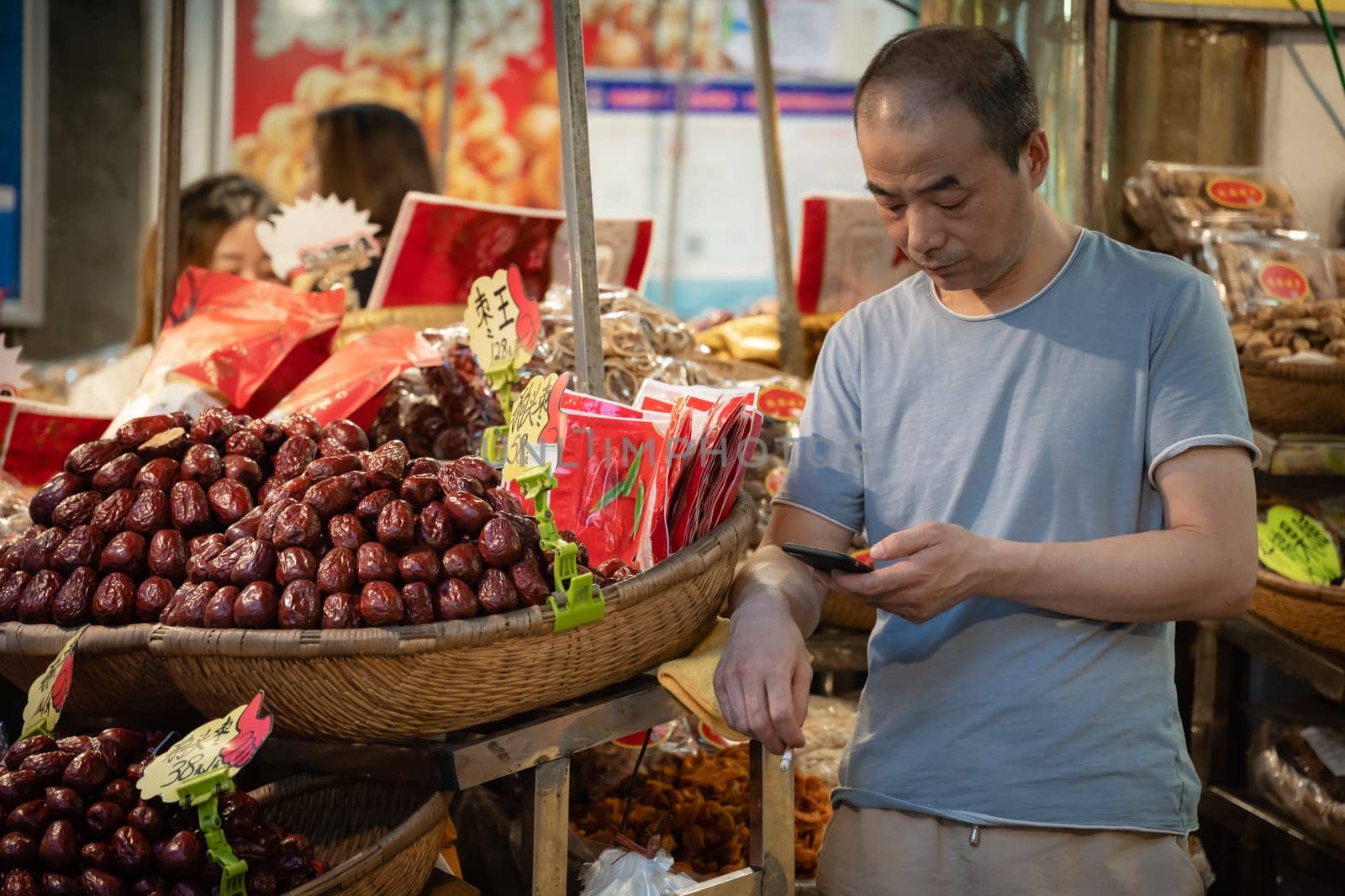 Xian, China -  July 2019 : Bored fruit seller checking his smartphone on a stall in Muslim Quarter