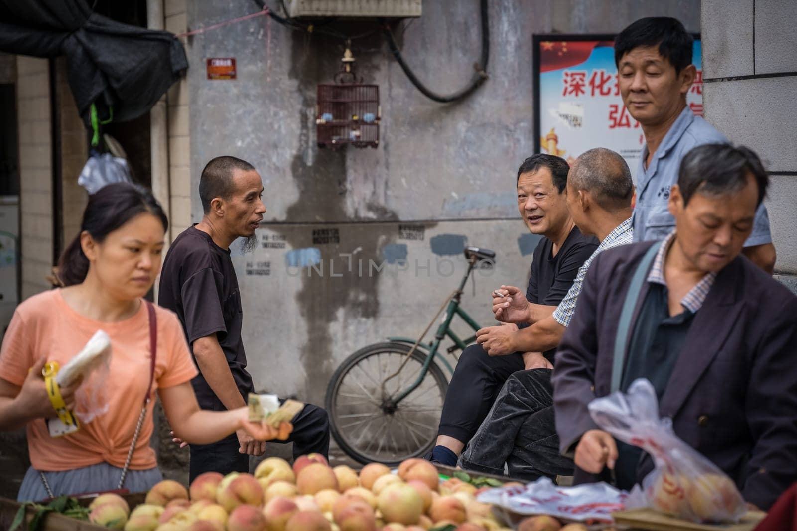 Xian, China -  July 2019 : Group of male friends talking and chatting behind a fruit stall in Muslim Quarter in Xian town, Shaanxi Province