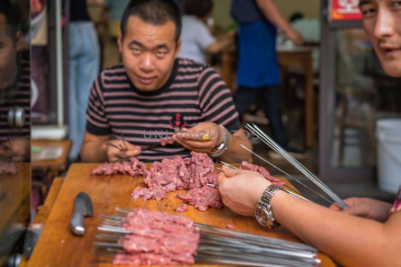 Xian, China -  July 2019 : Two men preparing sticks with pork and beef meat for kebabs to sell on the street in the Muslim Quarter