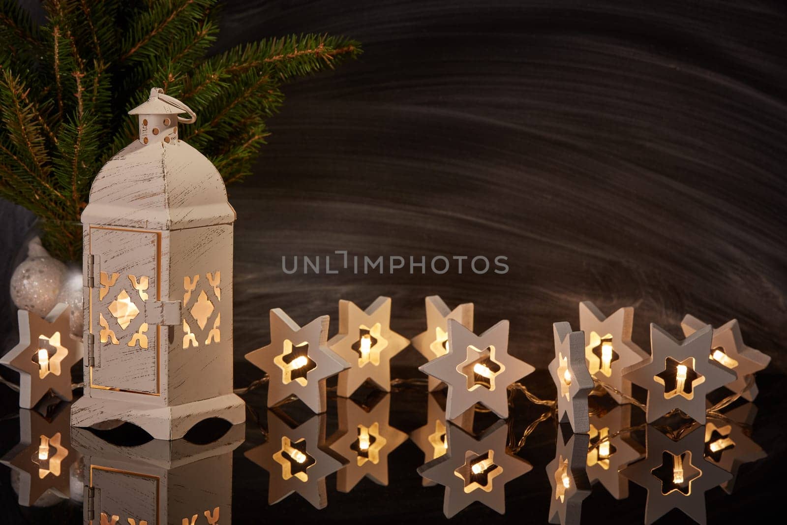 Decorative LED lights garland, fir branch and candle lantern on a black background with reflection. New Year and Christmas background with copy space. For greeting card or advertising