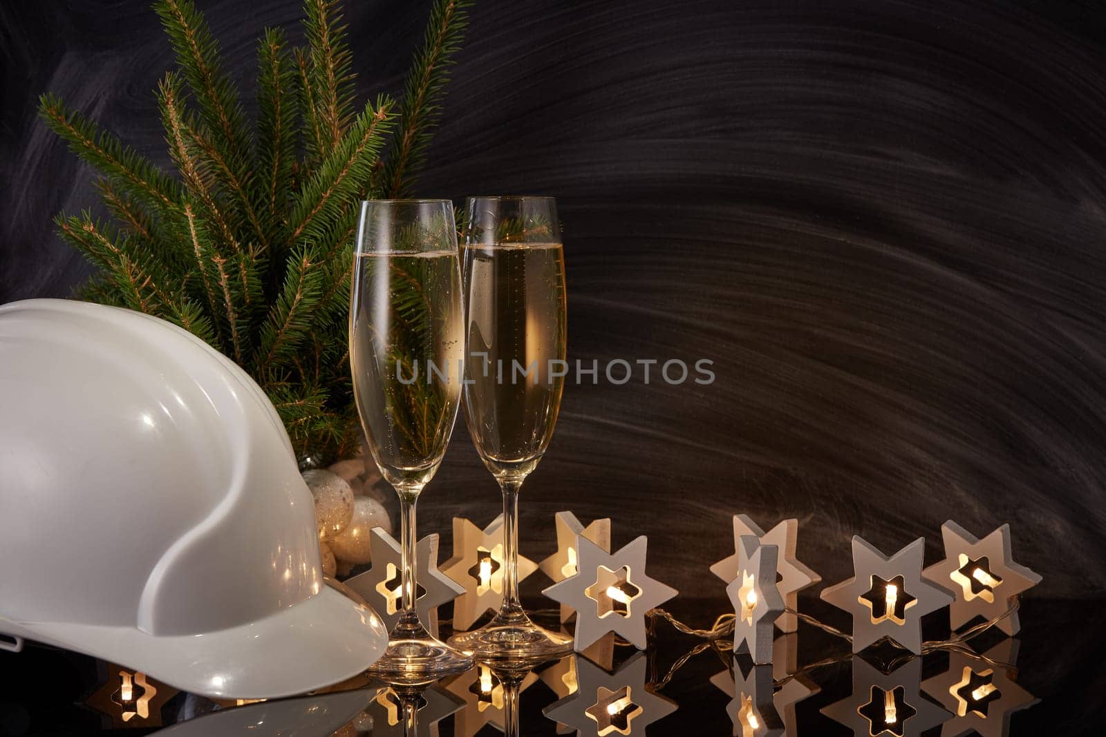 Construction hard hat, wineglasses with champagne and Christmas ornament on black background. Construction New Year, Christmas background with copy space. For greeting card or advertising