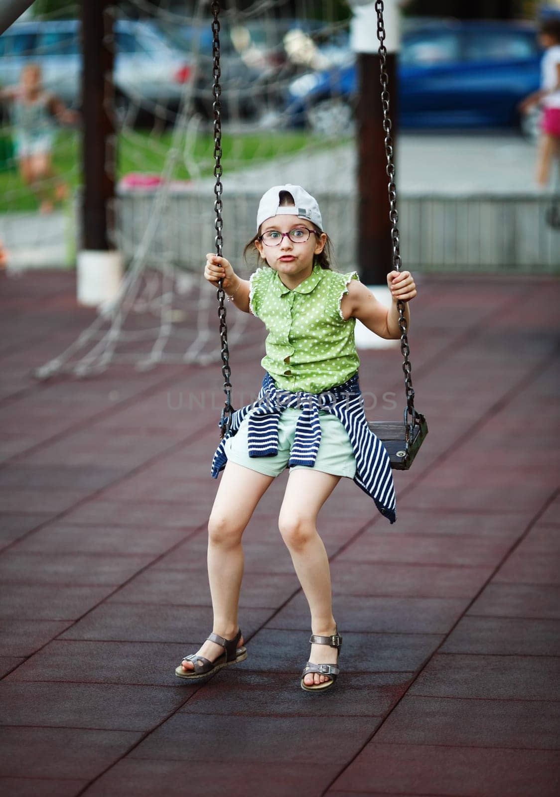 Child girl is swinging on a swing on the playground. Selective focus.