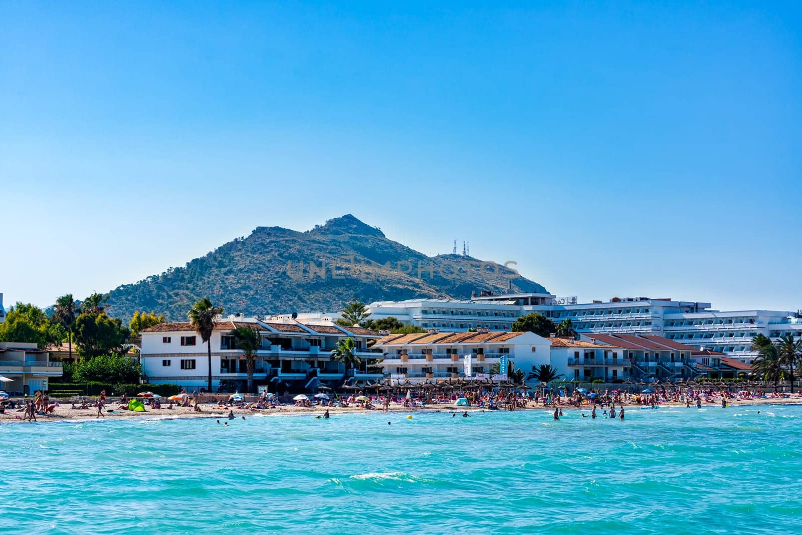 Mallorca, Spain, June 2015 People, tourists enjoying sun holidays on Alcudia beach, view from turquoise sea on sandy beach and mountain in background