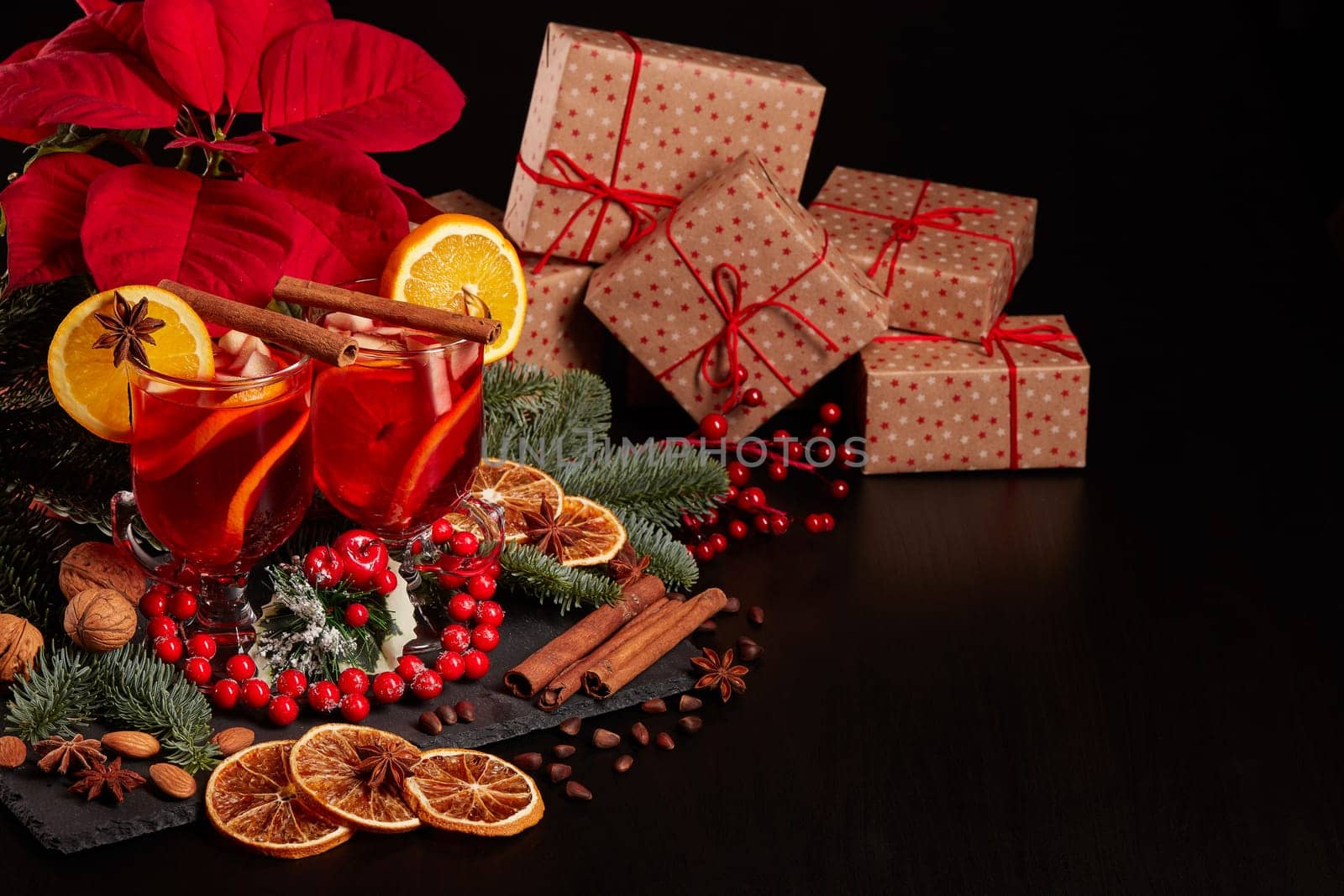 Still life with glasses of mulled wine or fruit tea, Red Poinsettia flowers, fir branch and gift boxes on a dark background with copy space. New year and Christmas table setting. Greeting card.