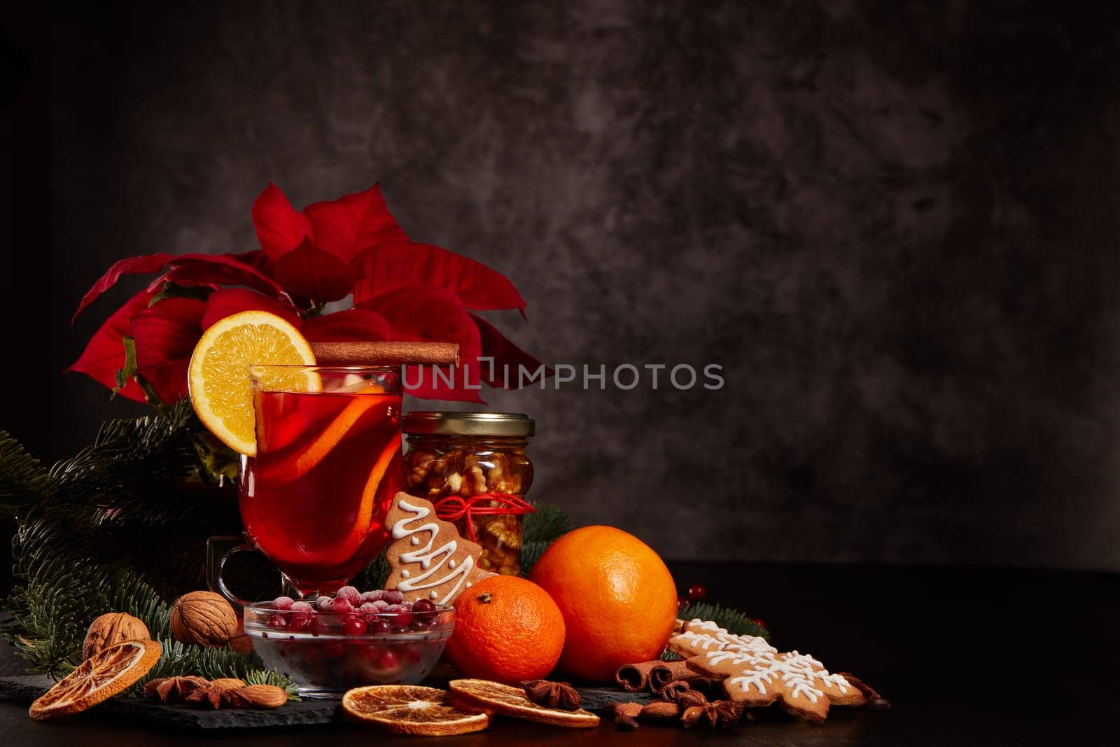 Still life with glasses of mulled wine or fruit tea, Red Poinsettia flowers, fir branch and spices on a dark background with copy space. New year and Christmas table setting. Greeting card.