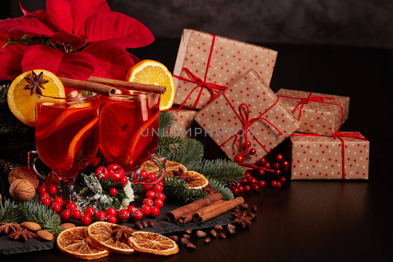 Still life with glasses of mulled wine or fruit tea, Red Poinsettia flowers, fir branch and gift boxes on a dark background with copy space. New year and Christmas table setting. Greeting card.