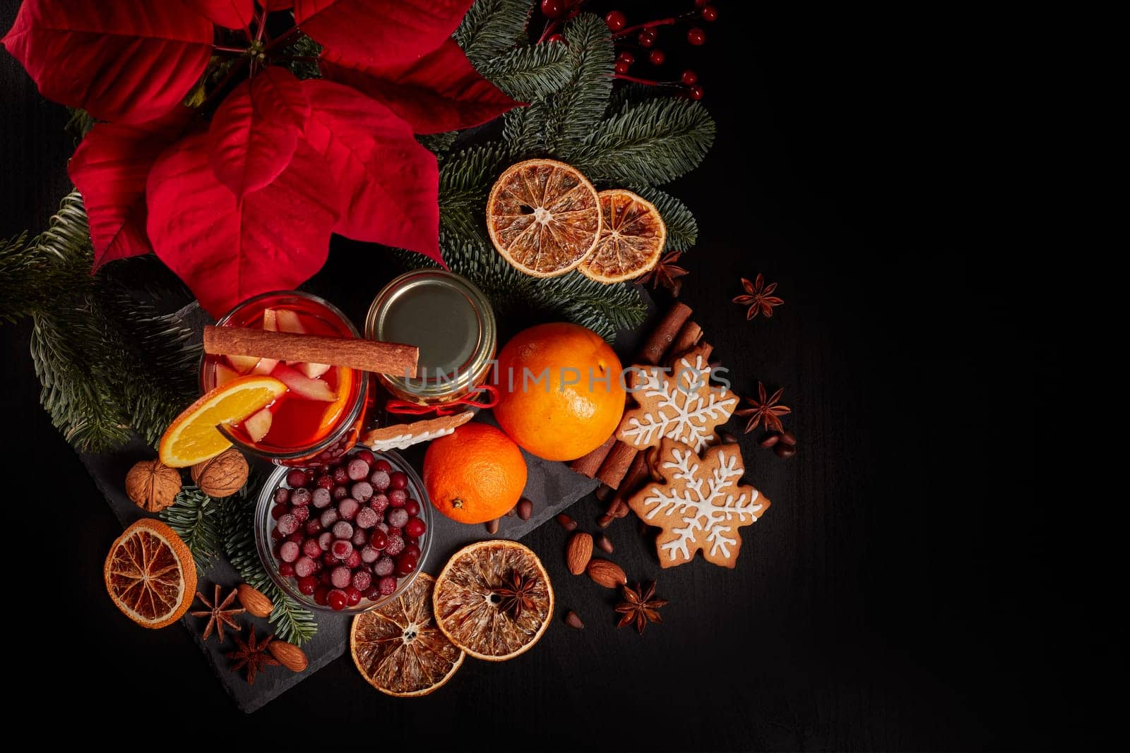 Still life with glasses of mulled wine or fruit tea, Red Poinsettia flowers, fir branch and spices on a dark background. Top view. New year and Christmas table setting. Greeting card.
