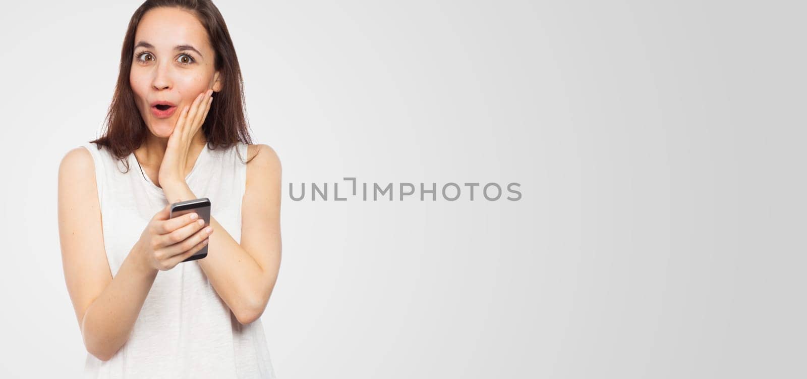 Young attractive woman looking surprised using her phone, looking at the camera