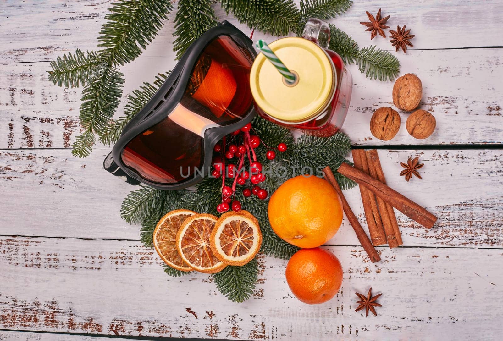 Winter holidays still life with fir tree branch, ski glasses, fruit tea, spices and oranges on a light wooden background. Top view. New Year and Christmas. Winter vacation.