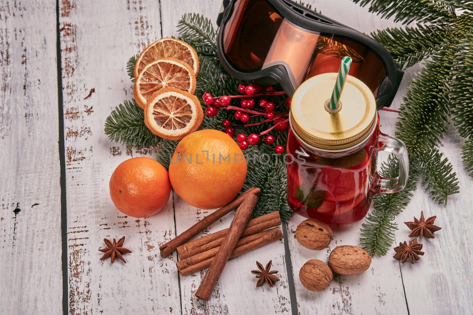 Winter holidays still life with fir tree branch, ski glasses, fruit tea, spices and oranges on a light wooden background. Top view with copy space. New Year and Christmas. Winter vacation.