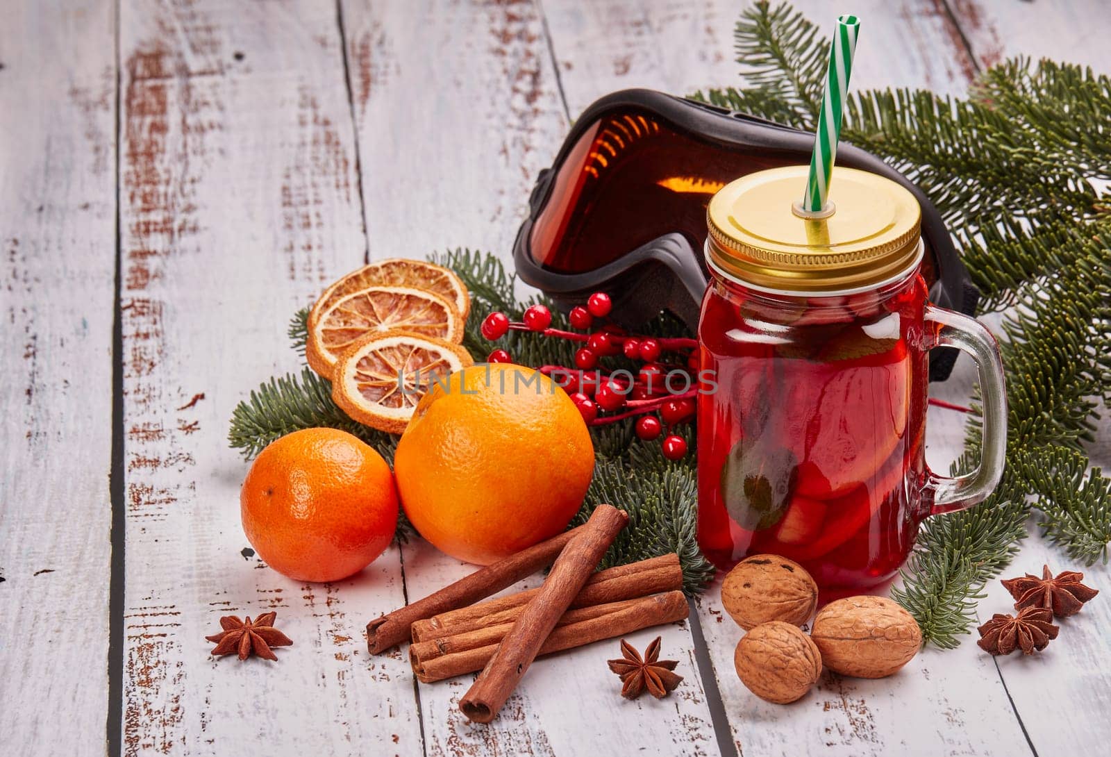 Winter holidays still life with fir tree branch, ski glasses, fruit tea, spices and oranges on a light wooden background with copy space. New Year and Christmas. Winter vacation.