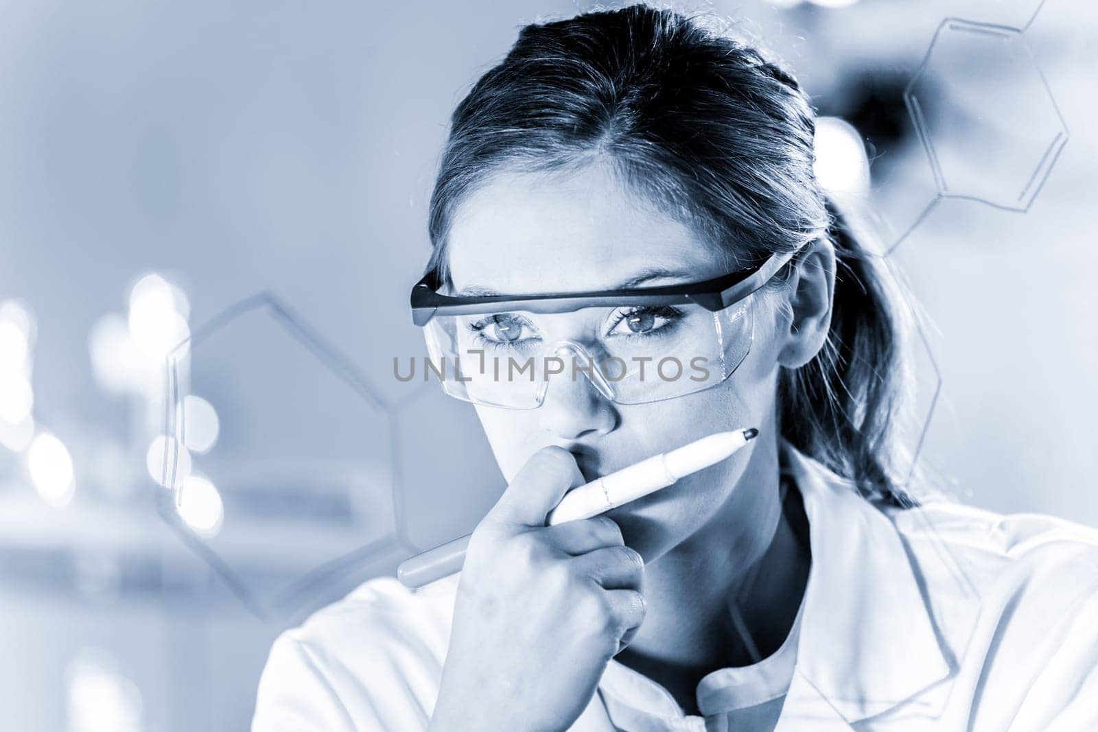 Portrait of a confident female health care expert in life science laboratory writing structural chemical formula on a glass board. Healthcare and modern life science concept. Blue toned image.