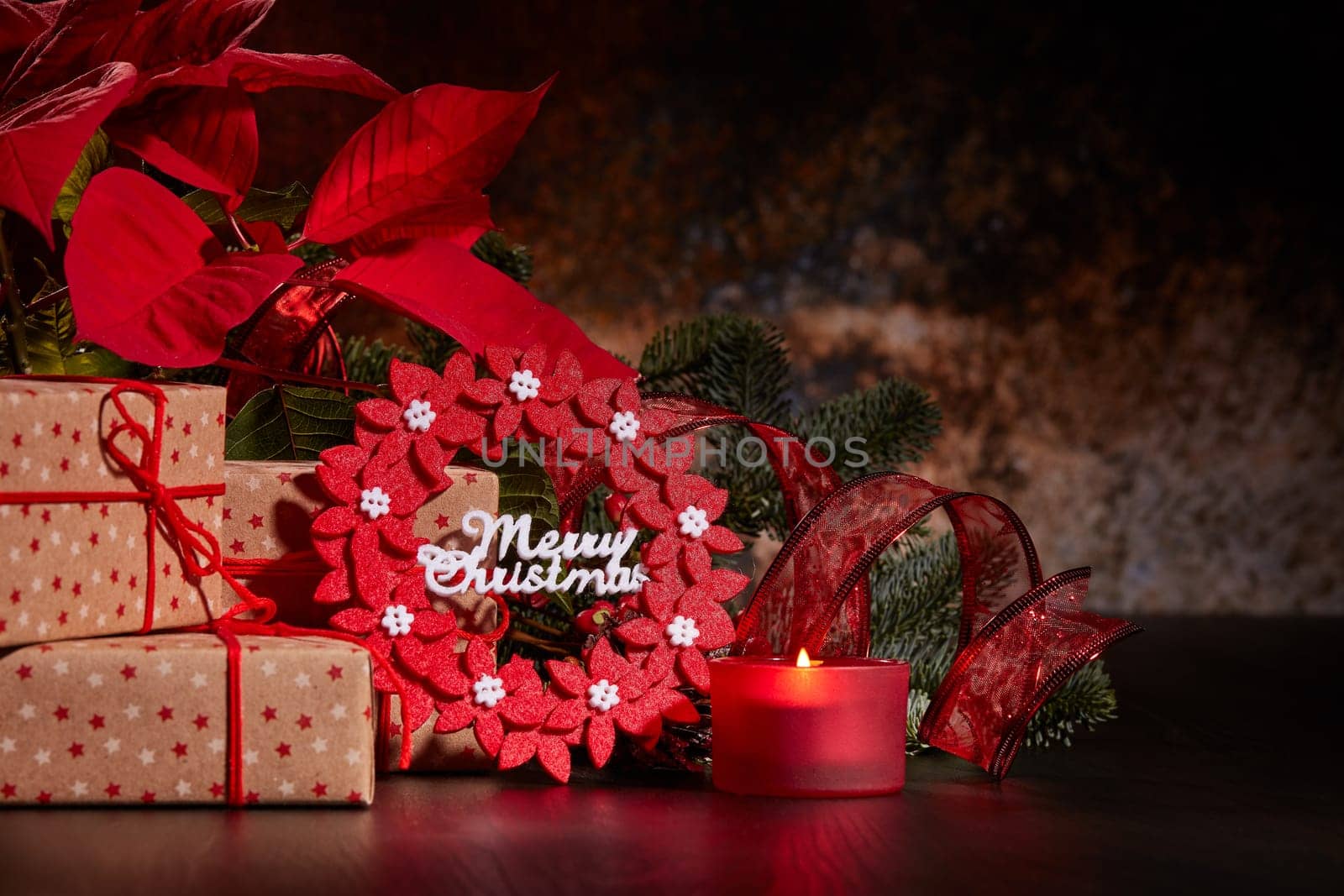 Christmas decoration with Red Poinsettia flowers (Euphorbia Pulcherrima), fir branch, burning candle and gift boxes on a dark background. Christmas background with copy space. Greeting card.