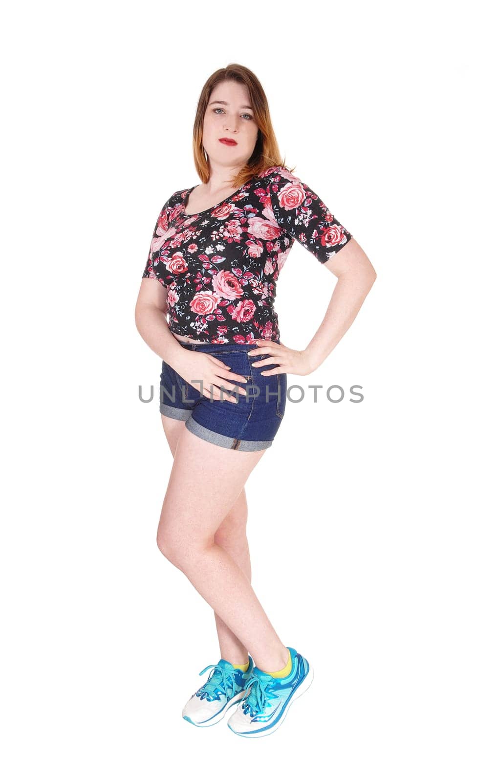 A lovely young woman standing in the studio in jeans shorts and a .colorful blouse and sneakers, isolated for white background.