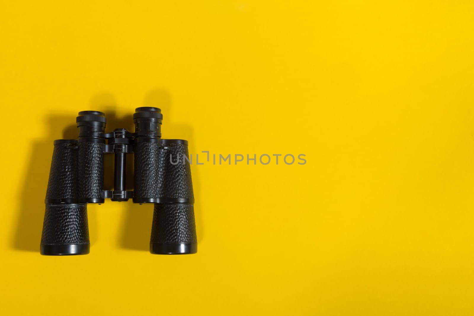 Black metalic binoculars on a yellow background