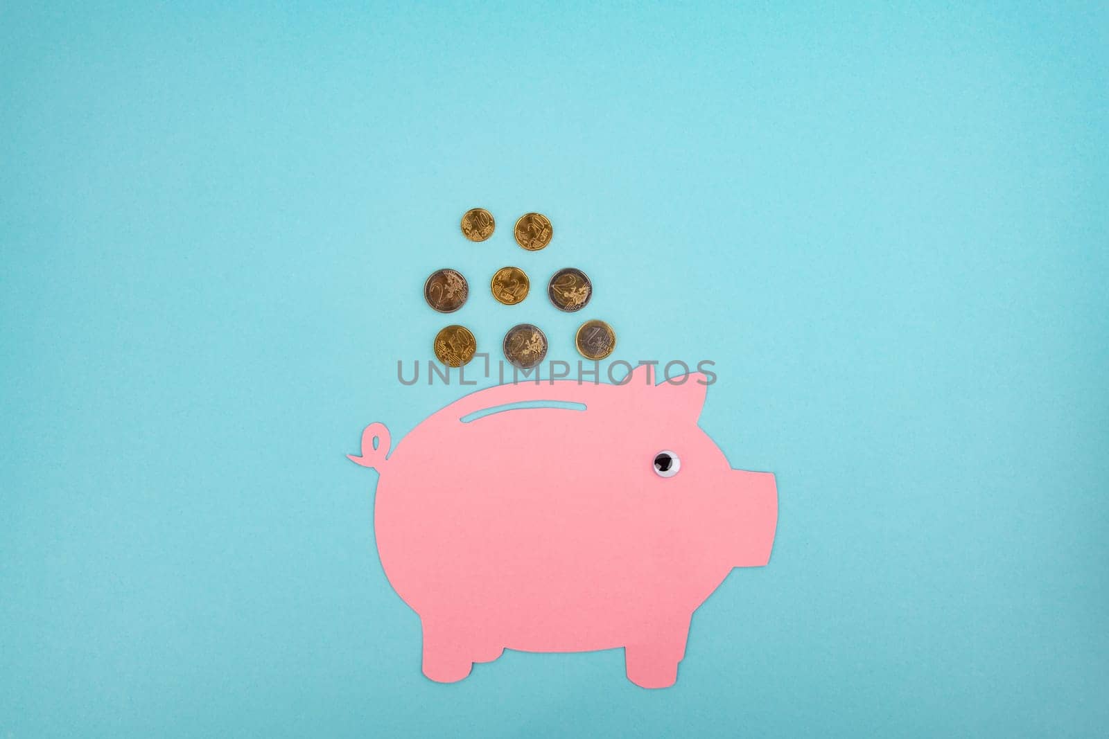 Cut out Paper Piggy Bank with Euro Coins on light Blue Background