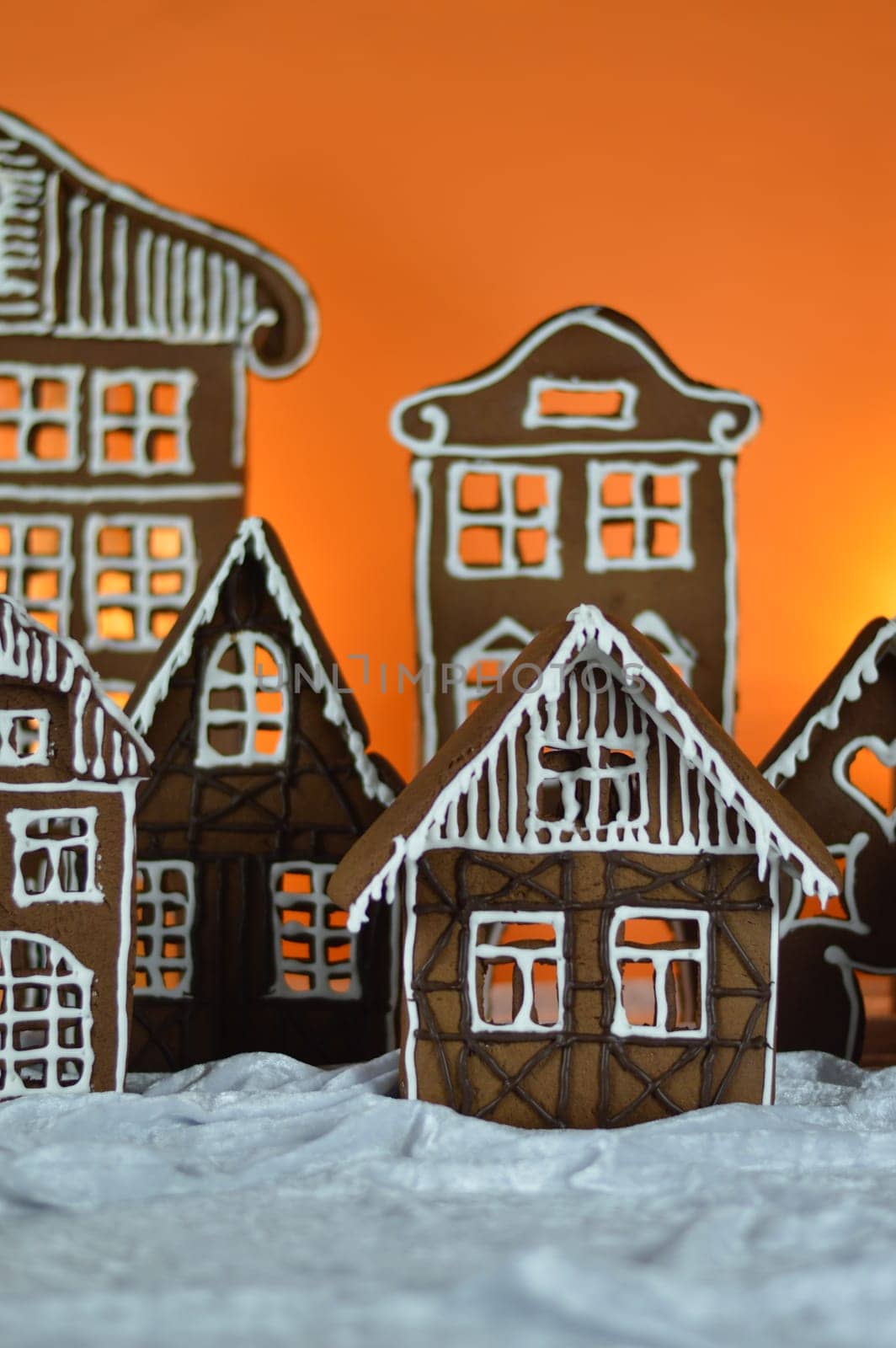 home made sweet delicious baked gingerbread village in front of orange background on white snowlike velvet as traditional christmas decoration for the family