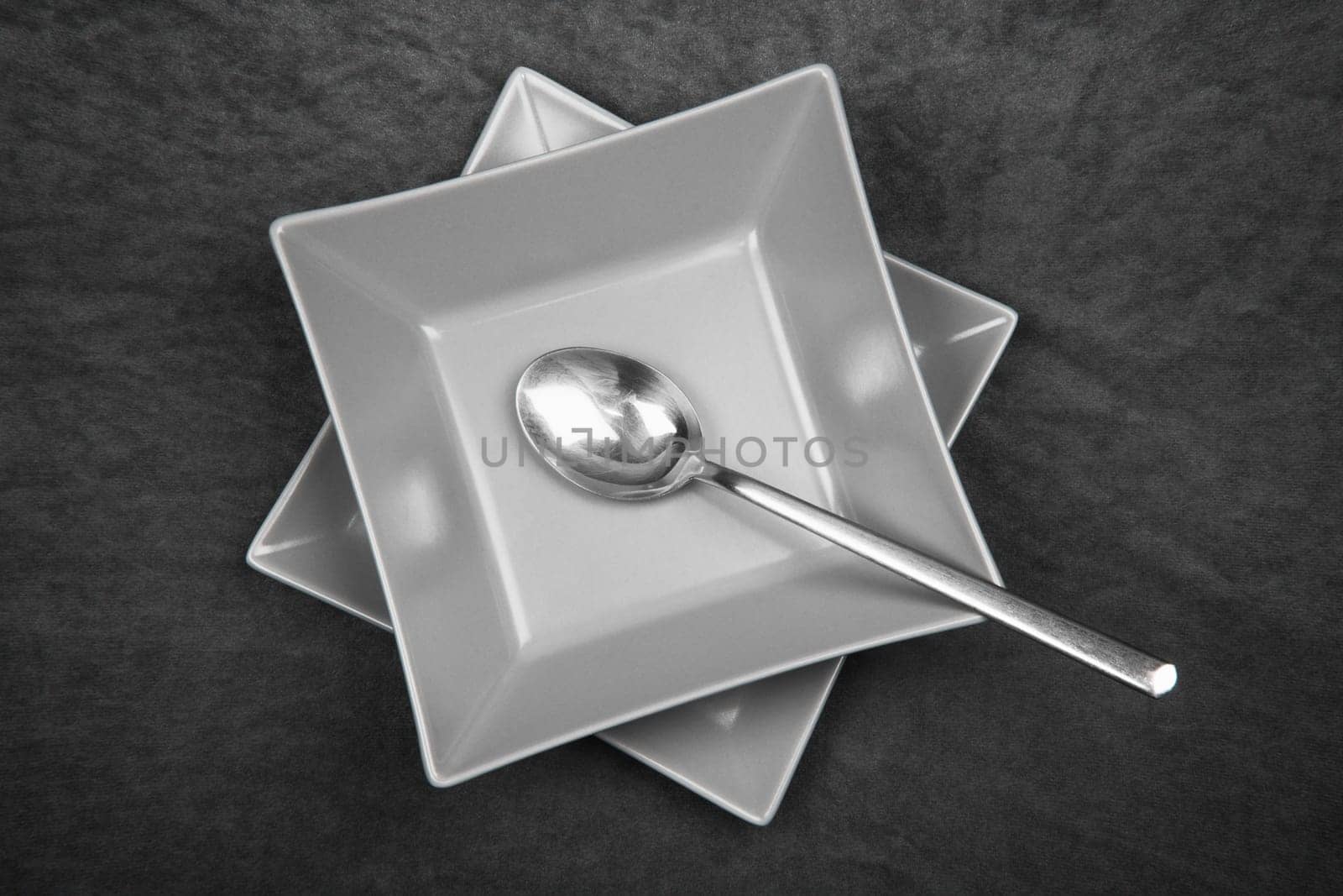 The gray square shaped table set with spoon is served on dark gray background.