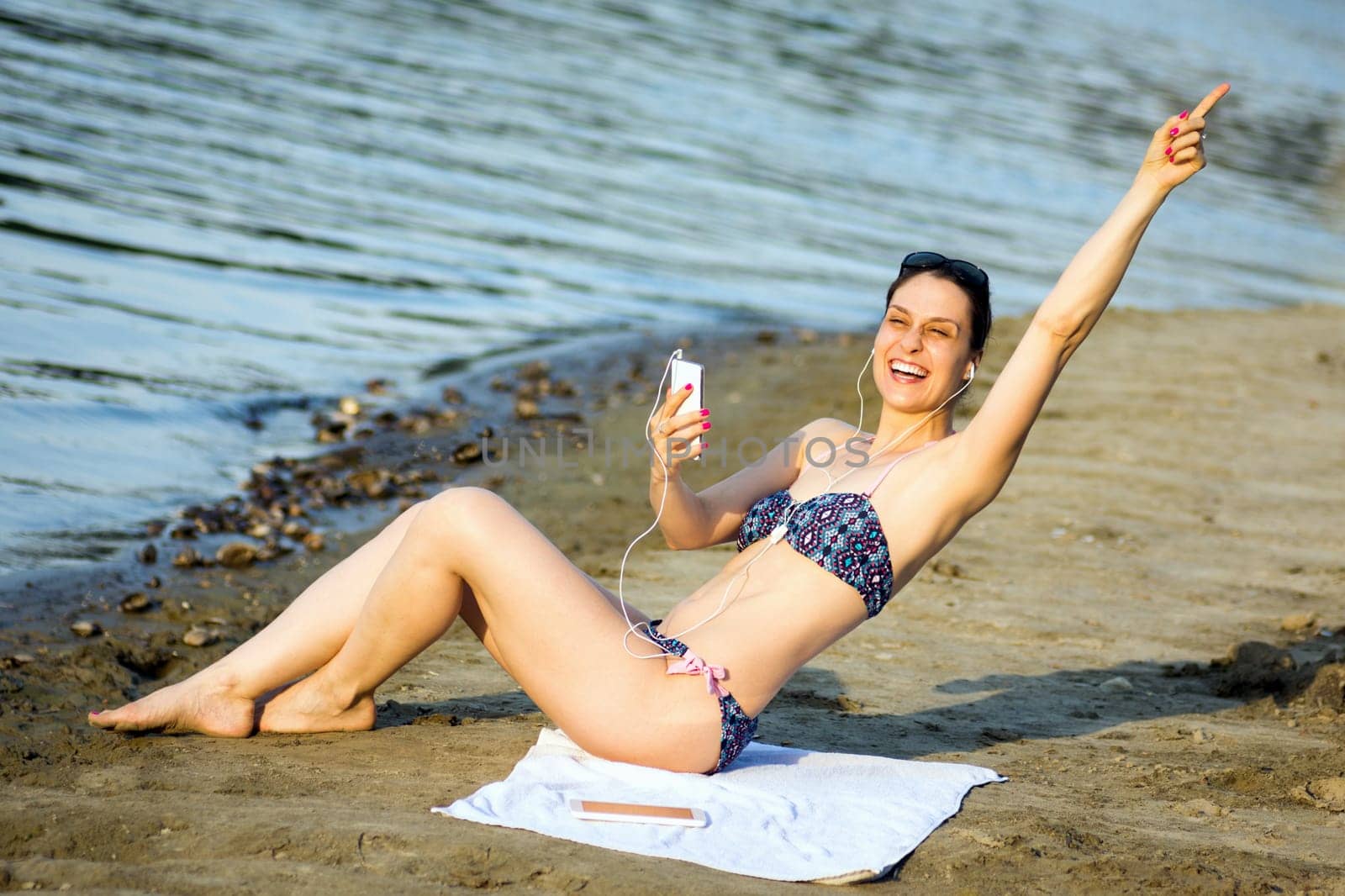 The attractive cheerful woman in bikini is having fun and using phone on the beach, summer lifestyle.