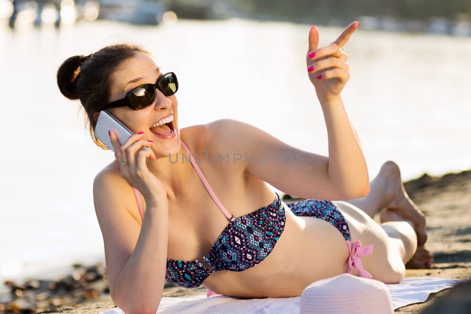 Sunbathing surprised woman in bikini is using phone on the beach, lifestyle at summer.