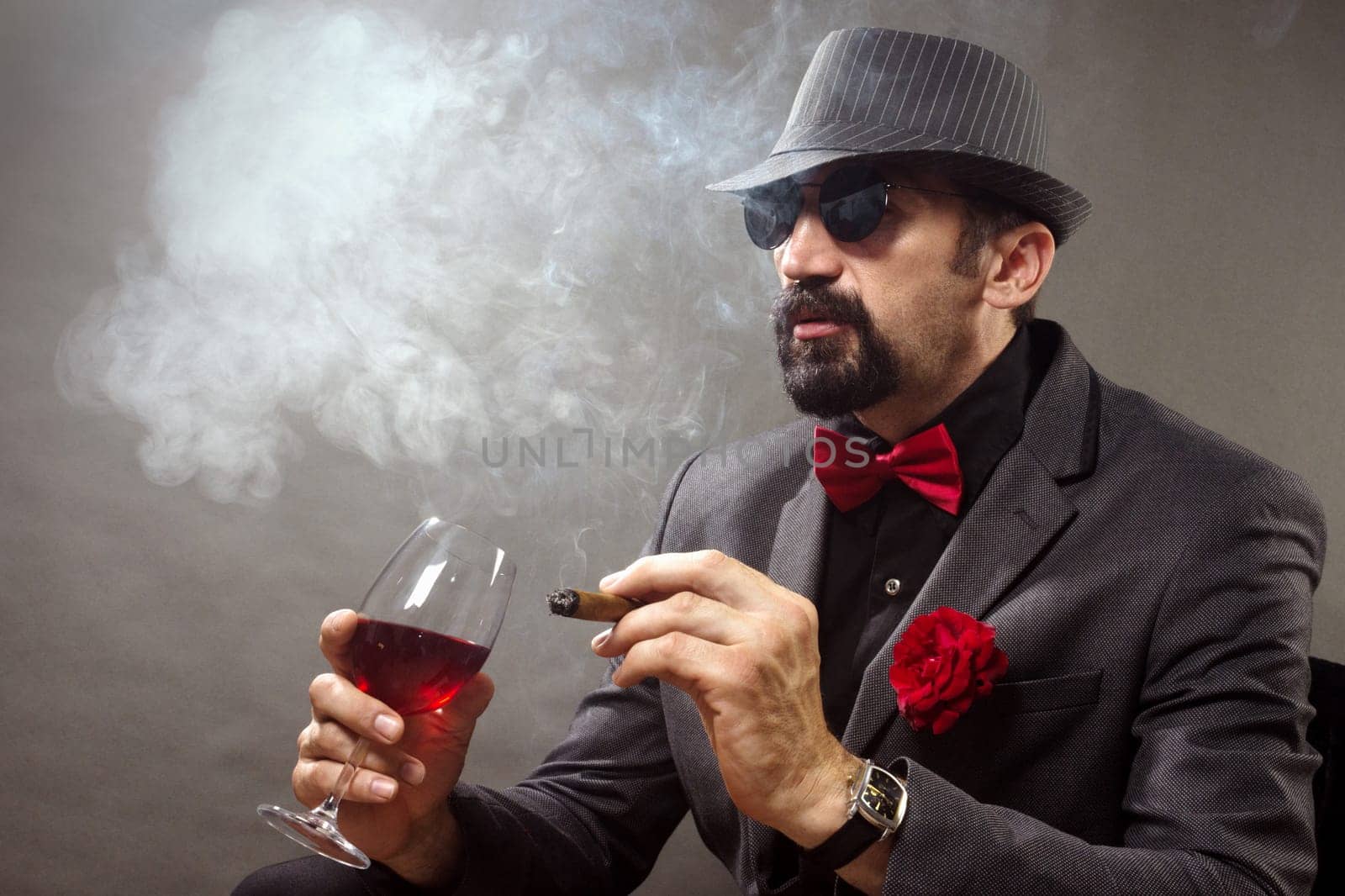 Elegant gentleman or mafia boss is smoking cigar and drinking red wine.