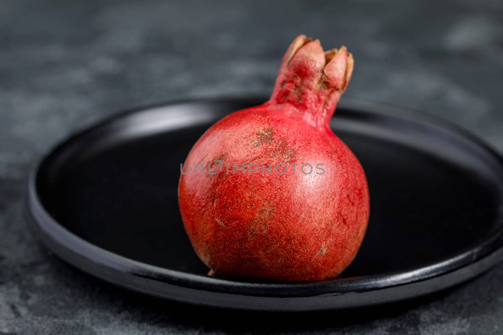 Pomegranate fruit on a red ceramic dish, whole, small, against a dark background