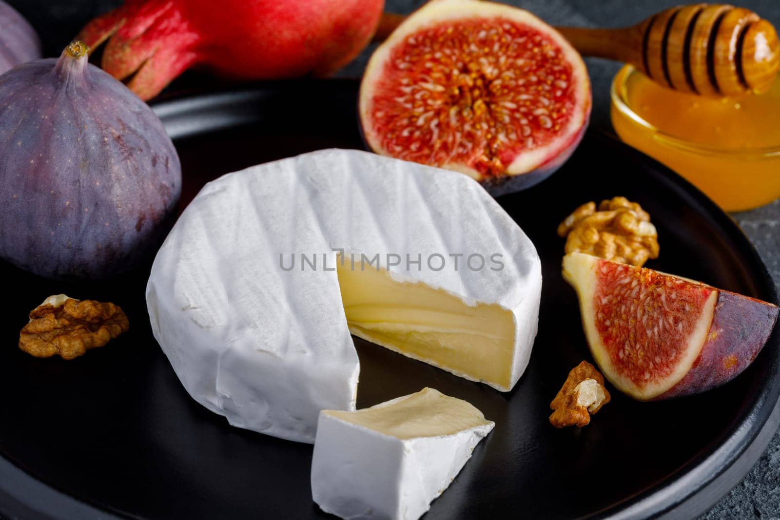 Camembert cheese on a ceramic dish with peeled walnuts and figs, honey and pomegranate