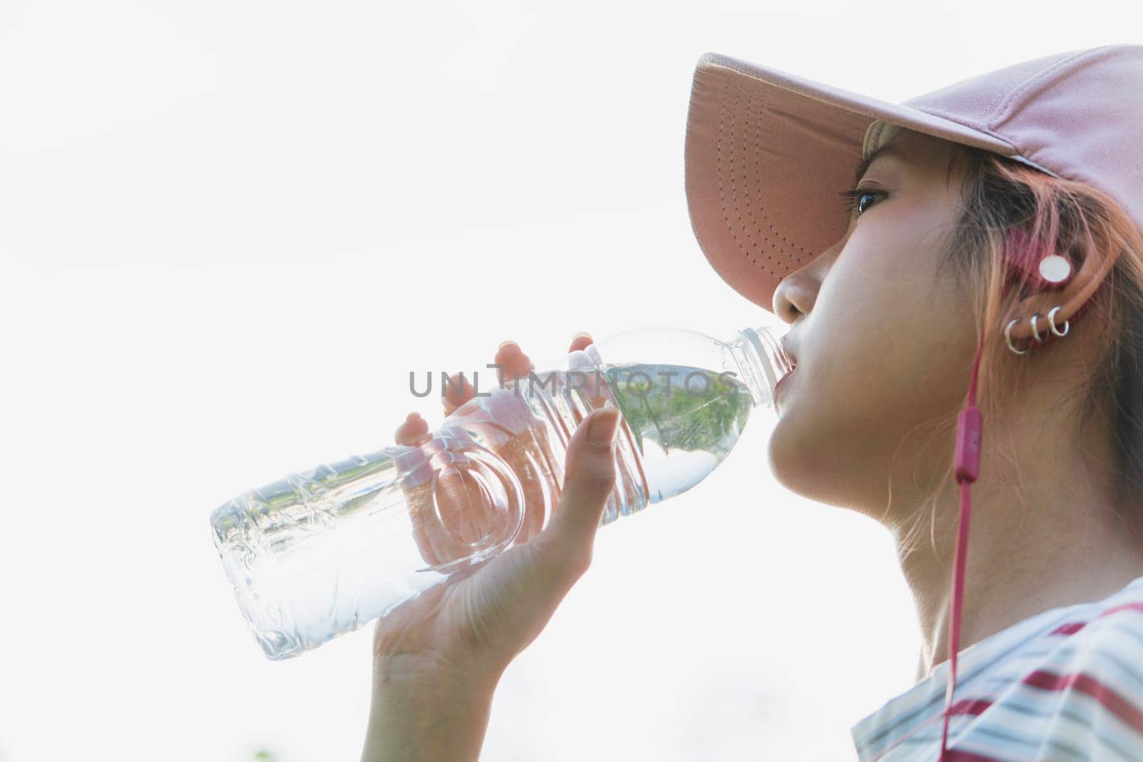 Close up of a woman drinking water from a bottle after exercise. Portrait of a woman drinking a water at outside.