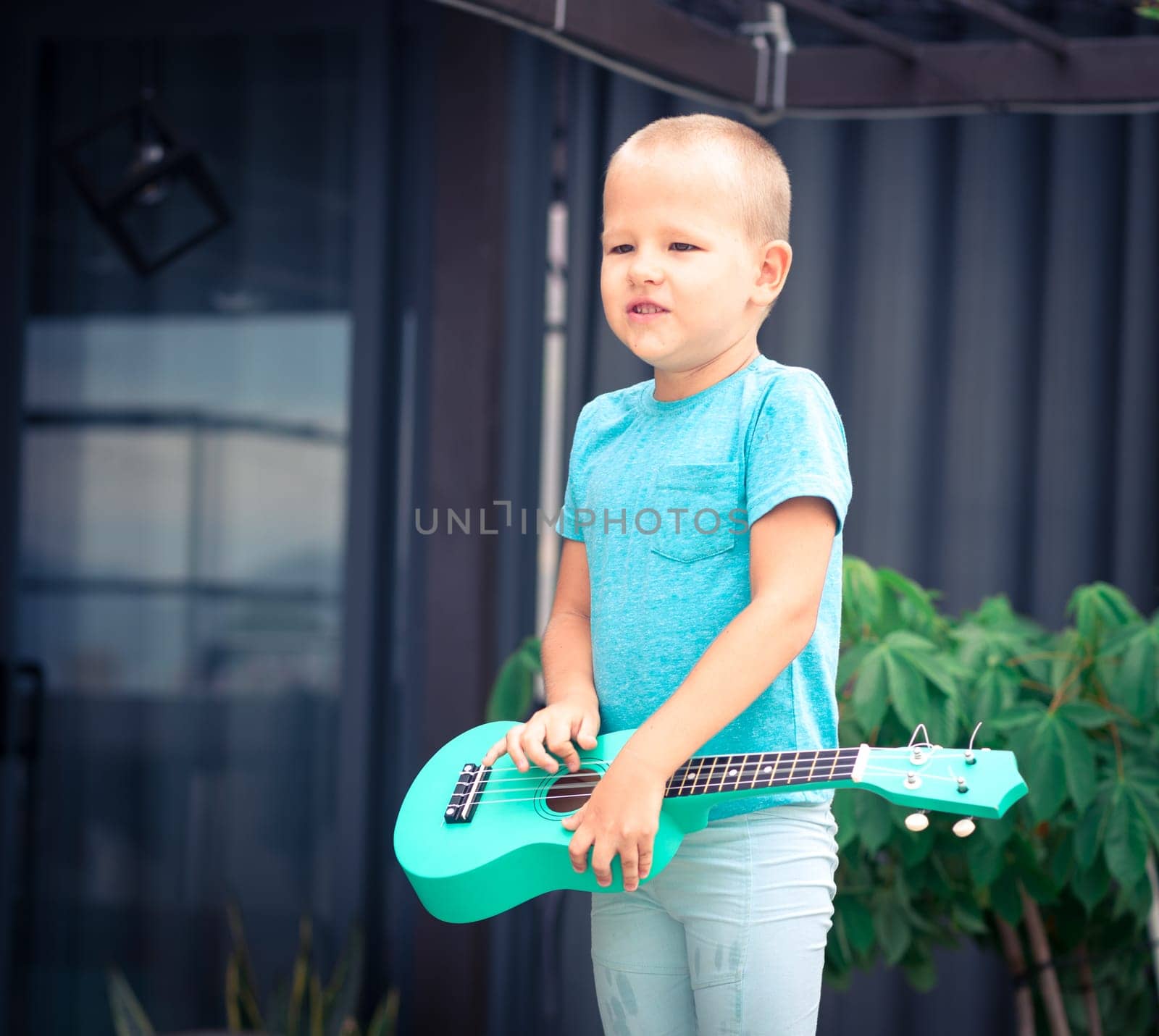 Portrait of a cute boy sitting ouddoor with ukulele