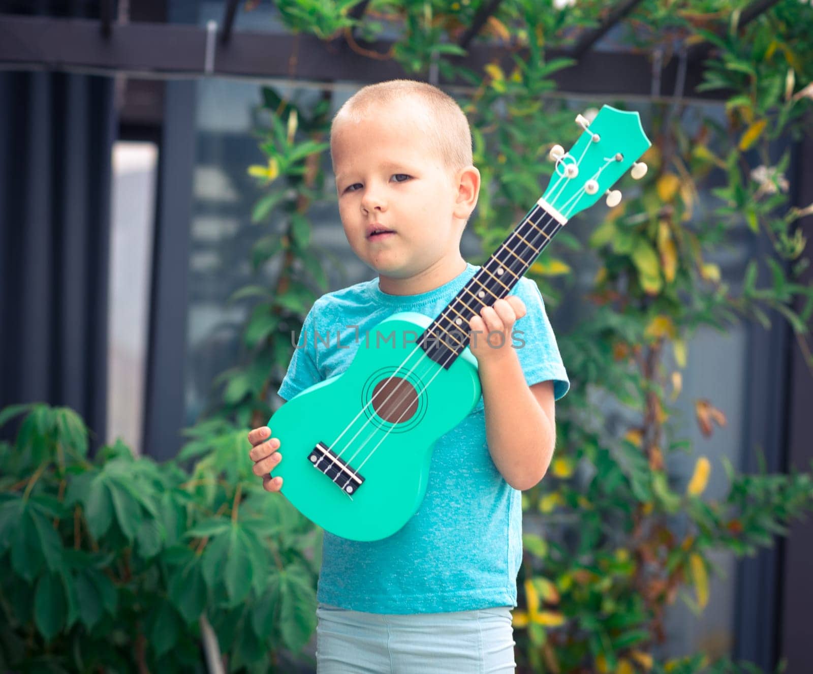 Portrait of a cute boy sitting ouddoor with ukulele