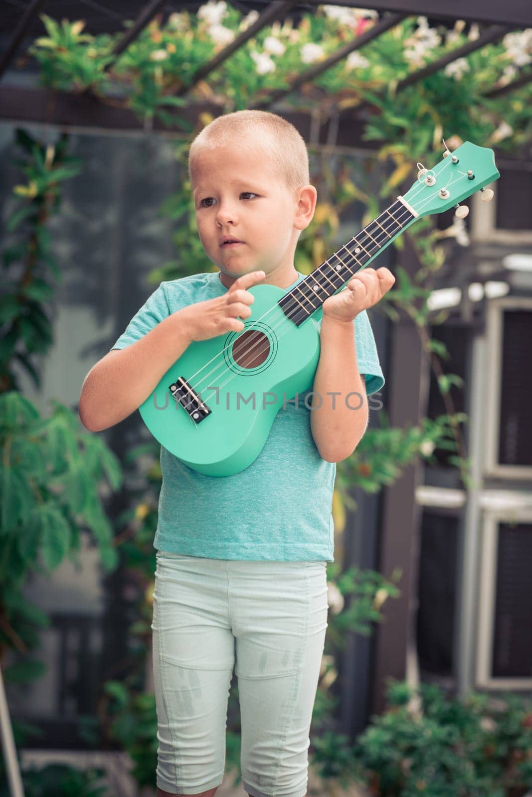 Portrait of a cute boy sitting ouddoor with ukulele