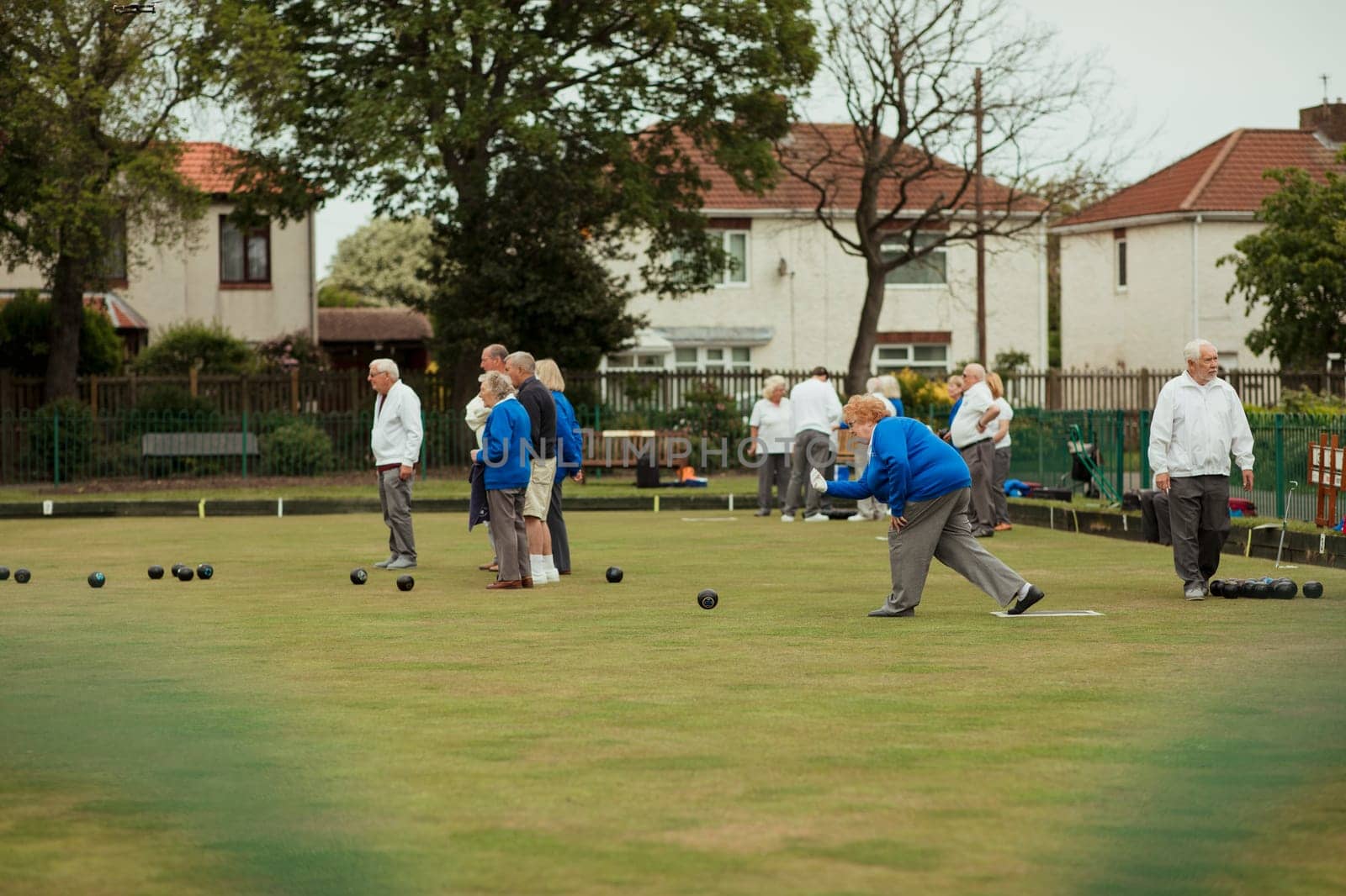 A side view shot of a senior woman taking her shot in a game of lawn bowling, surrounded by other seniors in the community.