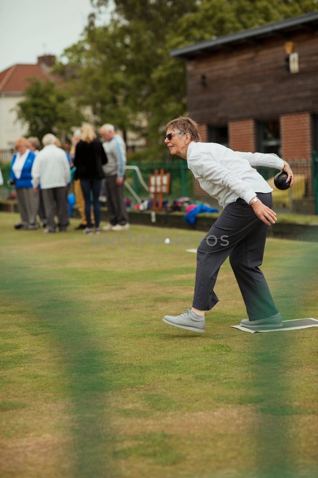 A side view shot of a senior woman taking her shot in a game of lawn bowling.