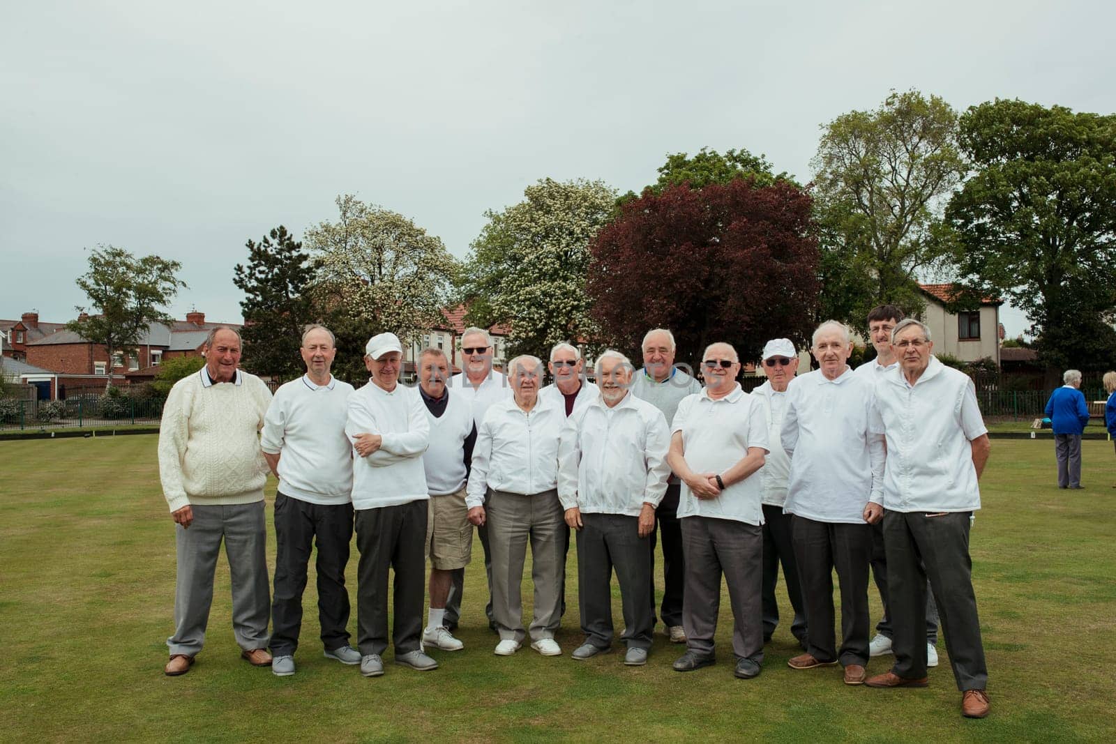 A front view shot of a community of senior men smiling at a bowling green.