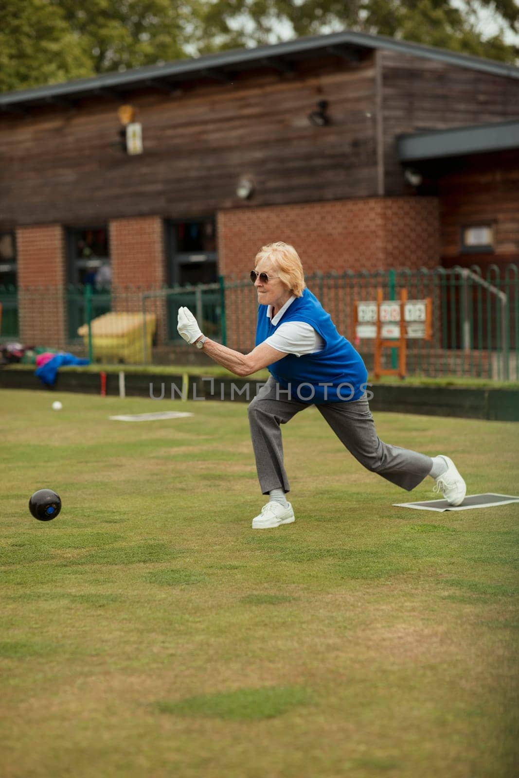 A side view shot of a senior woman taking her shot in a game of lawn bowling.