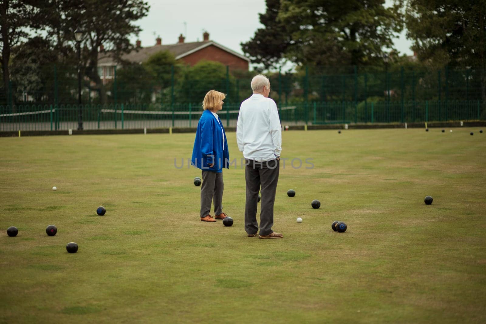 Two senior adults standing together in the middle of a bowling green, surrounded by bocce balls.