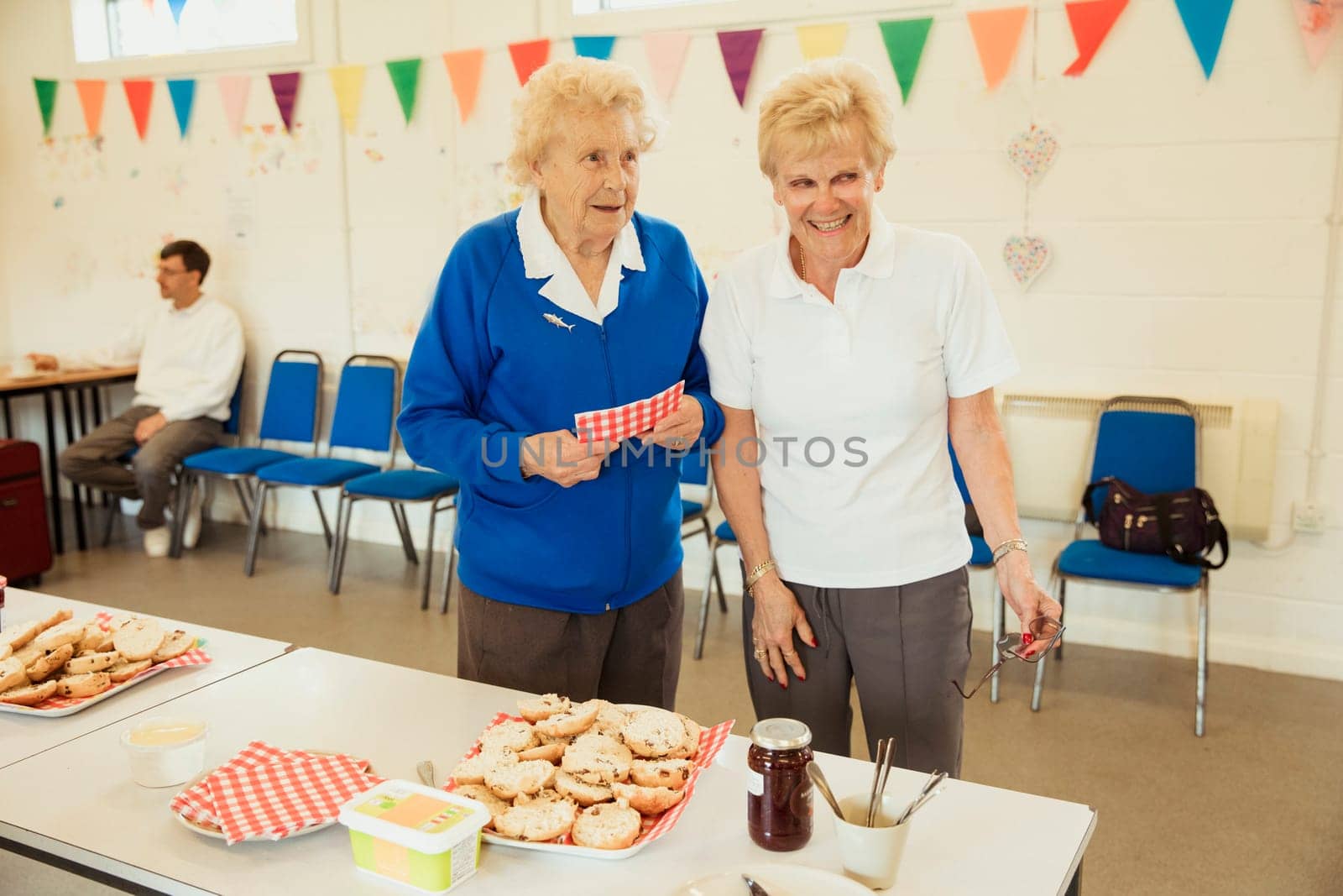 A front view shot of two senior friends selling scones at a bake sale.