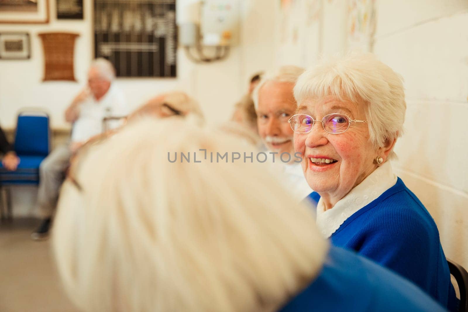 A clsoe up shot of a senior woman sitting with friends, looking at the camera.